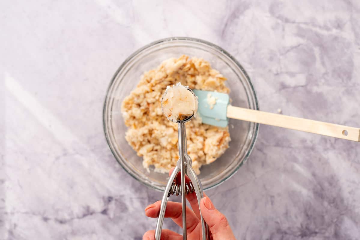 Cookie dough in a bowl on the bench with one scooped cookie portion