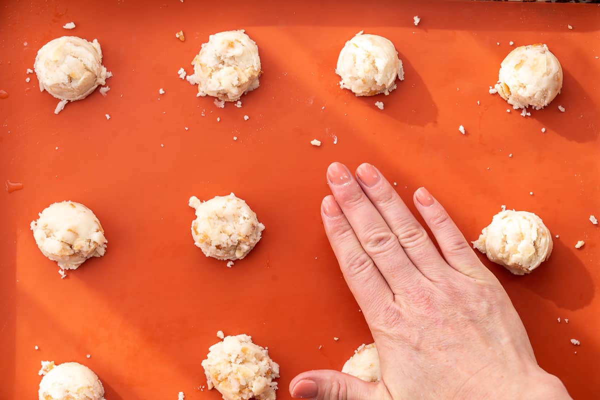Cookies portioned on a lined baking paper with one hand pressing one cookie