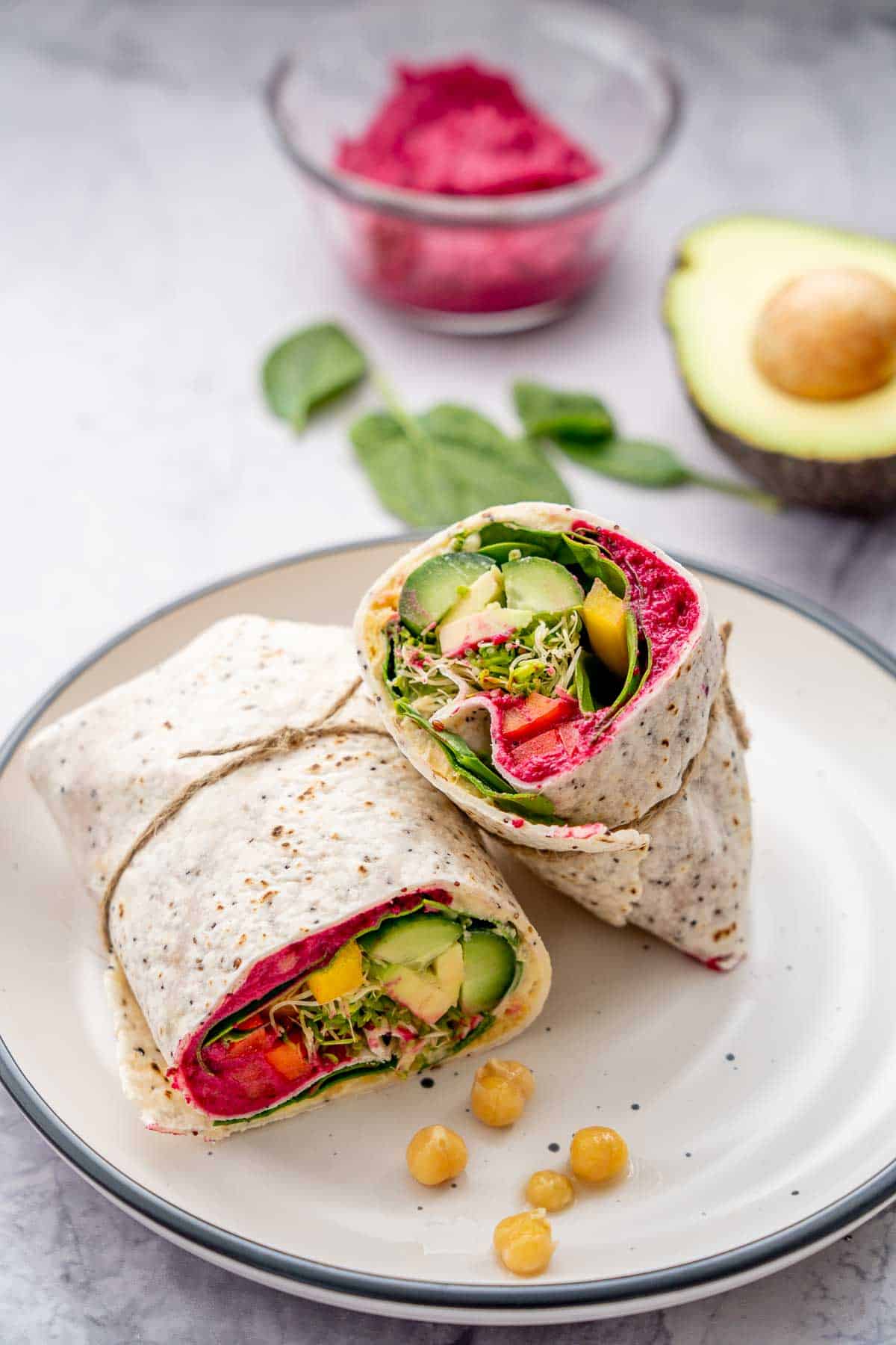 Halved filled wrap stuffed with beetroot hummus, cucumber, sprouts, spinach and capsicum sitting on a dish on a bench