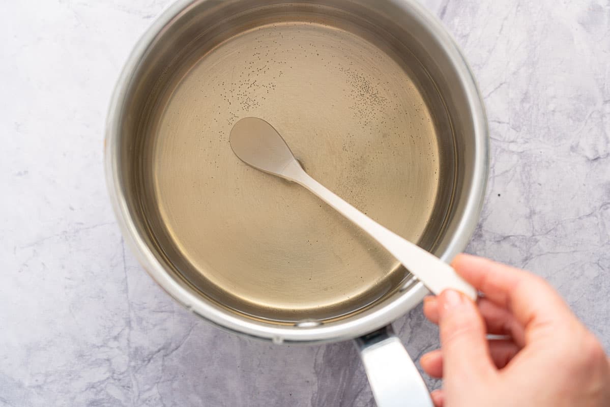 Vinegar, water, sugar, salt in a pot being stirred with spoon.