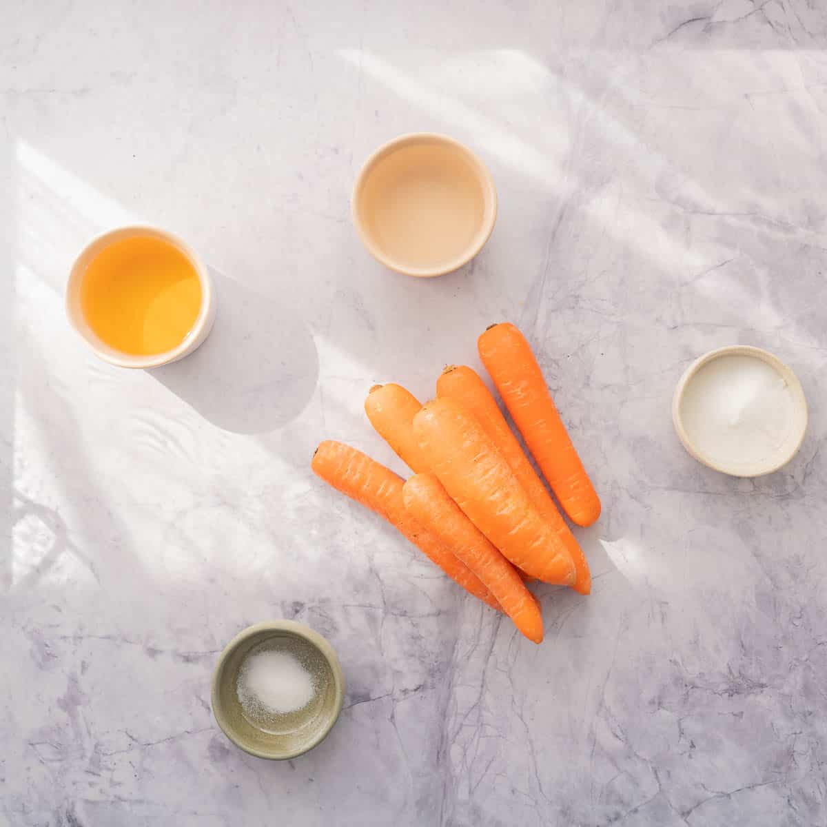 Stack of whole carrots, sitting next to individual ramekins of apple cider vinegar, salt, sugar and water