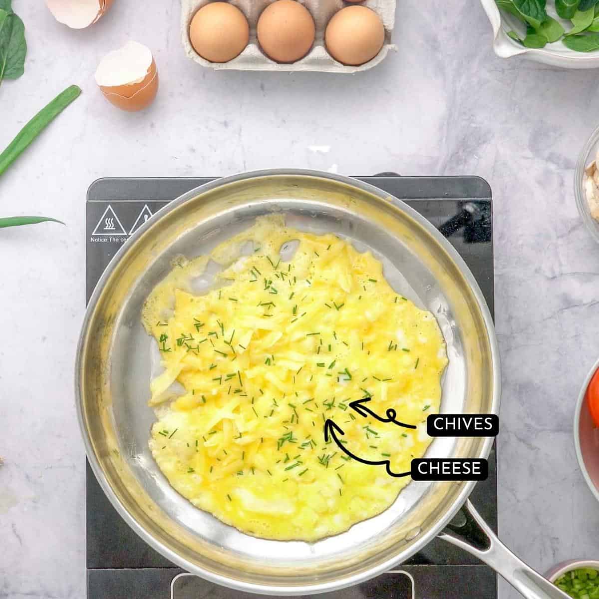 Rice paper omelette in pan with text overlay and arrows pointing too ingredients inside, chives and cheese.
