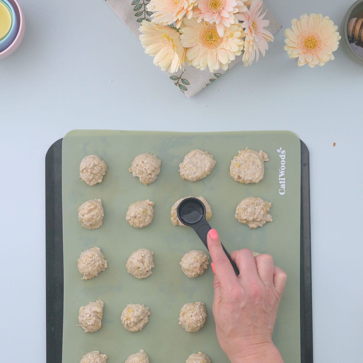 A hand using a black measuring scoop to flatten cookies.