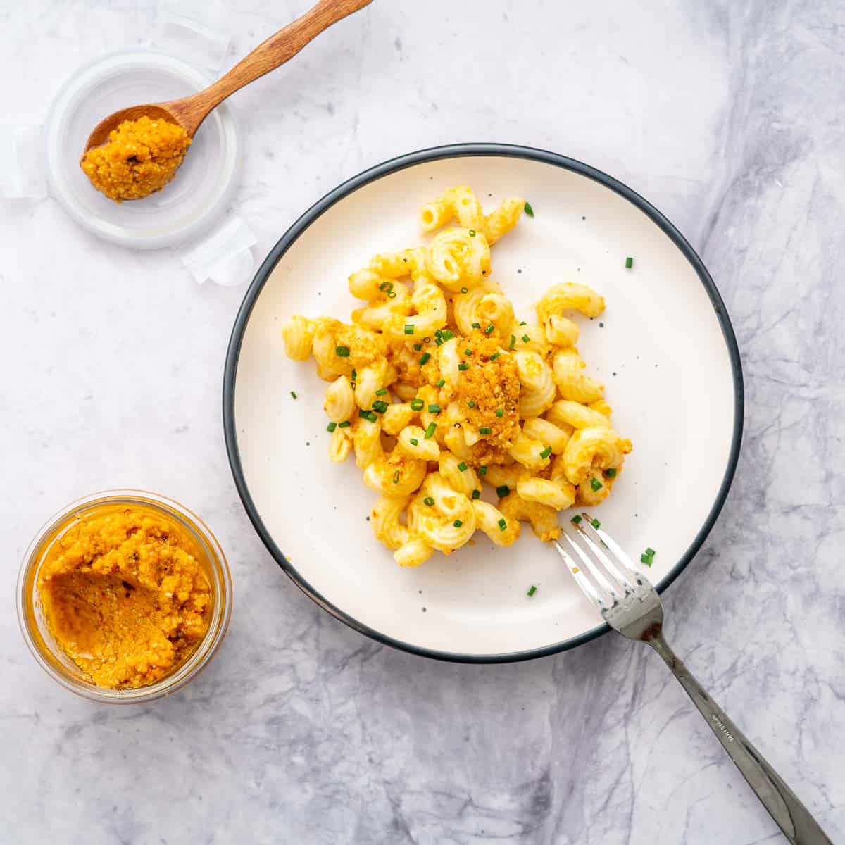 A plate of carrot pesto pasta next to a jar of carrot pesto.