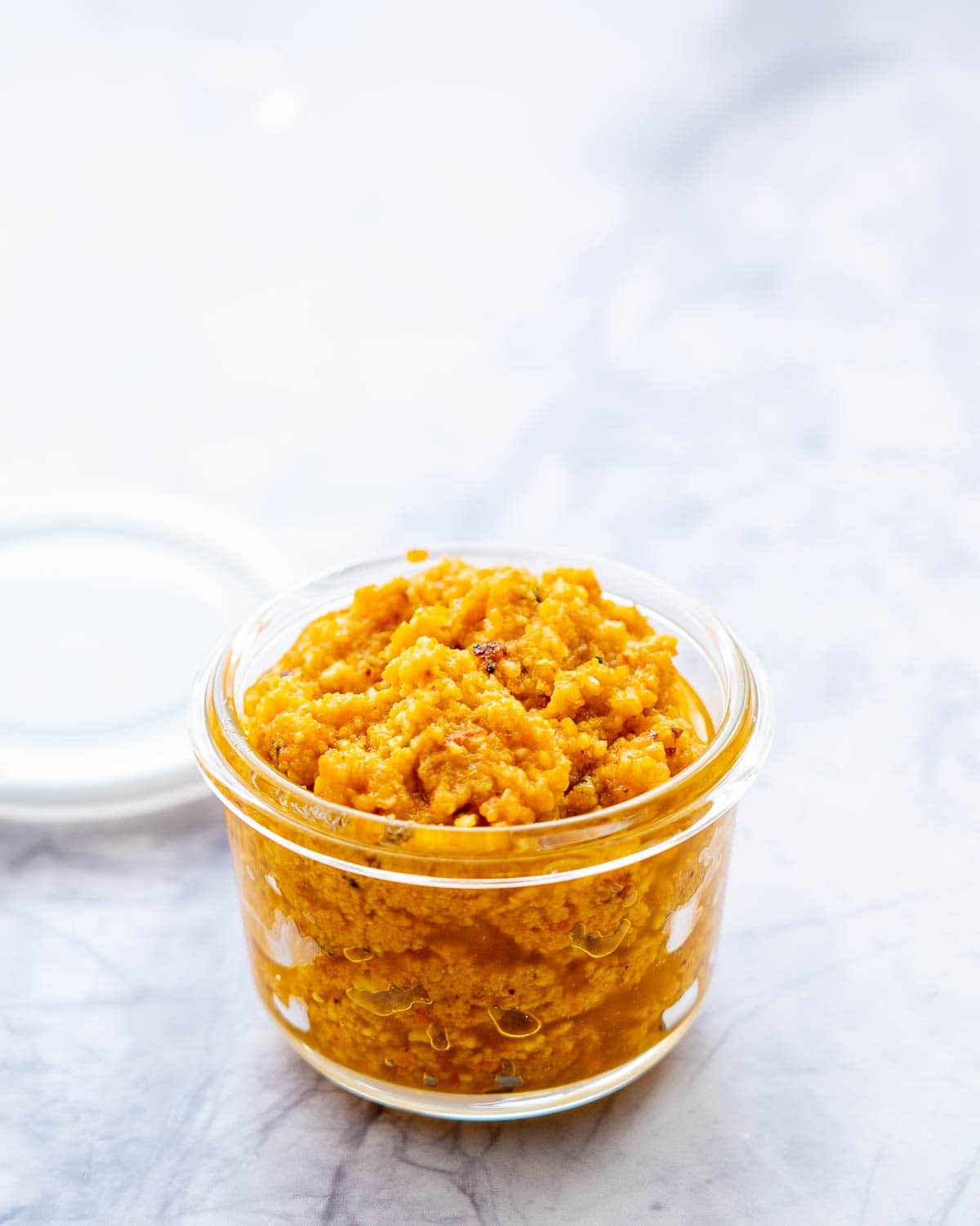 A small glass jar filled with orange pesto on a grey marble bench.