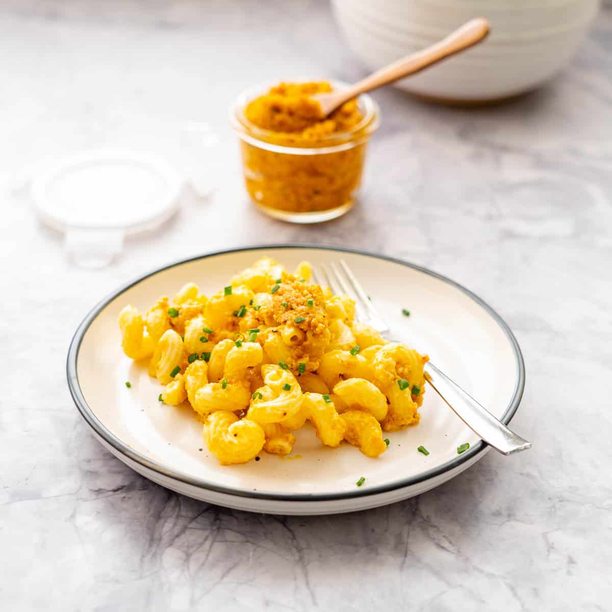 A plate of pasta topped with orange pesto sauce and garnished with chopped chives.