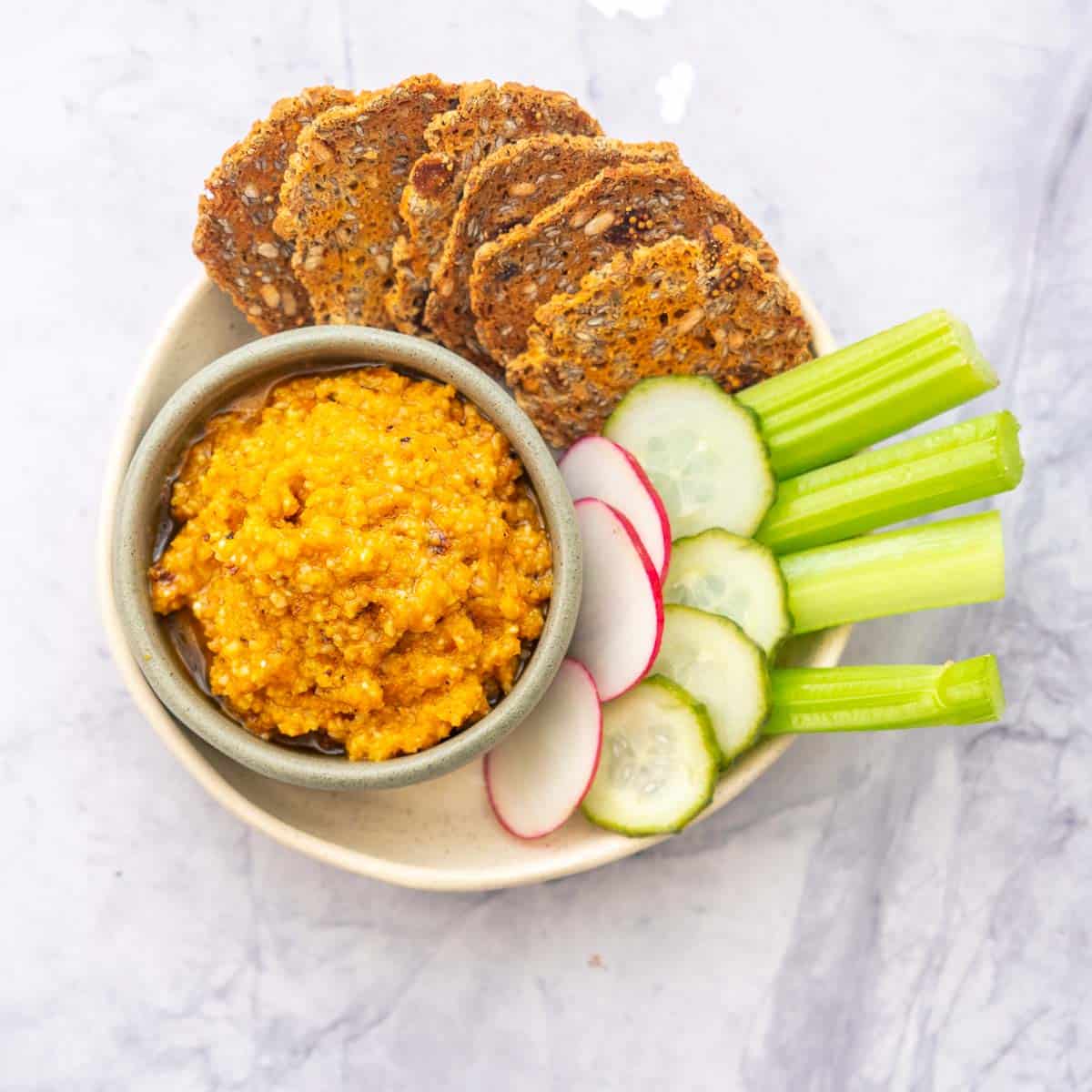 A snack platter of sliced vegetables, carakers and orange carrot pesto.
