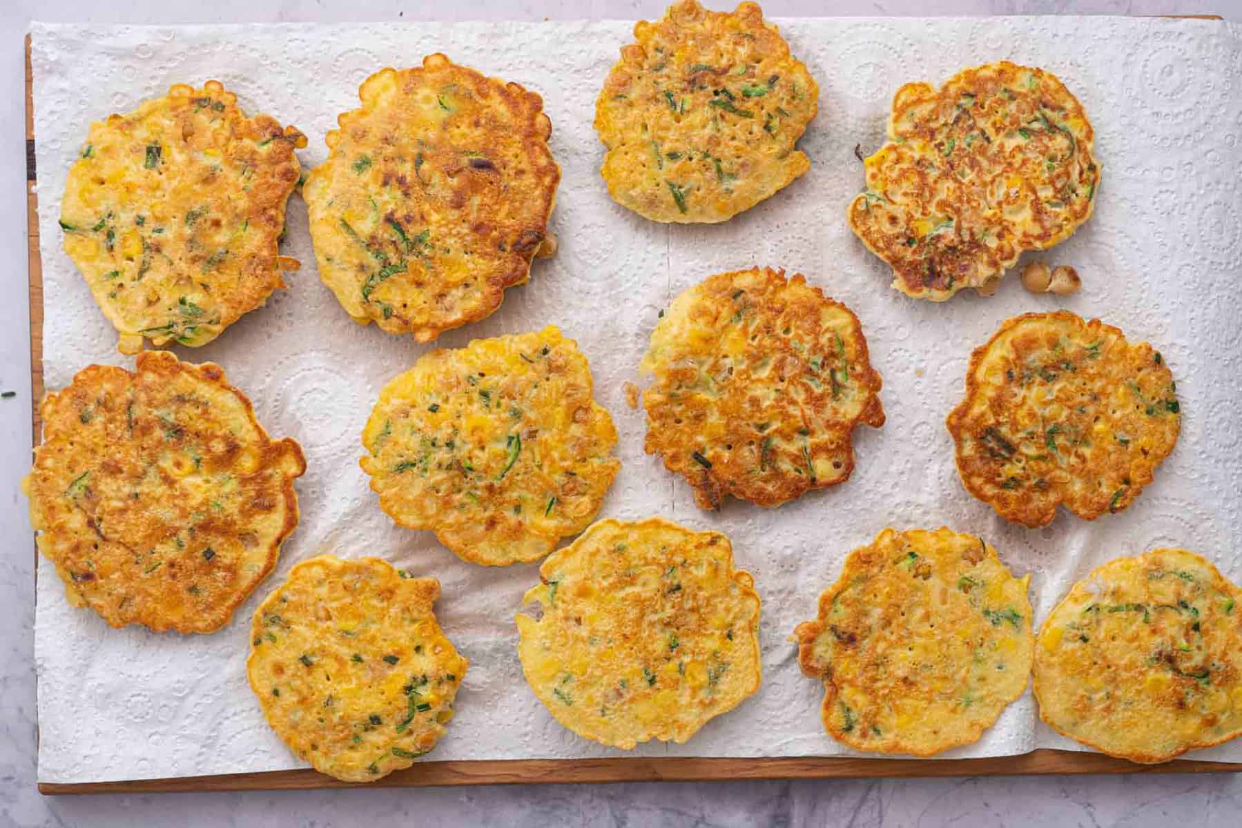 twelve golden brown chickpea fritters resting on chopping board with a sheet of kitchen roll