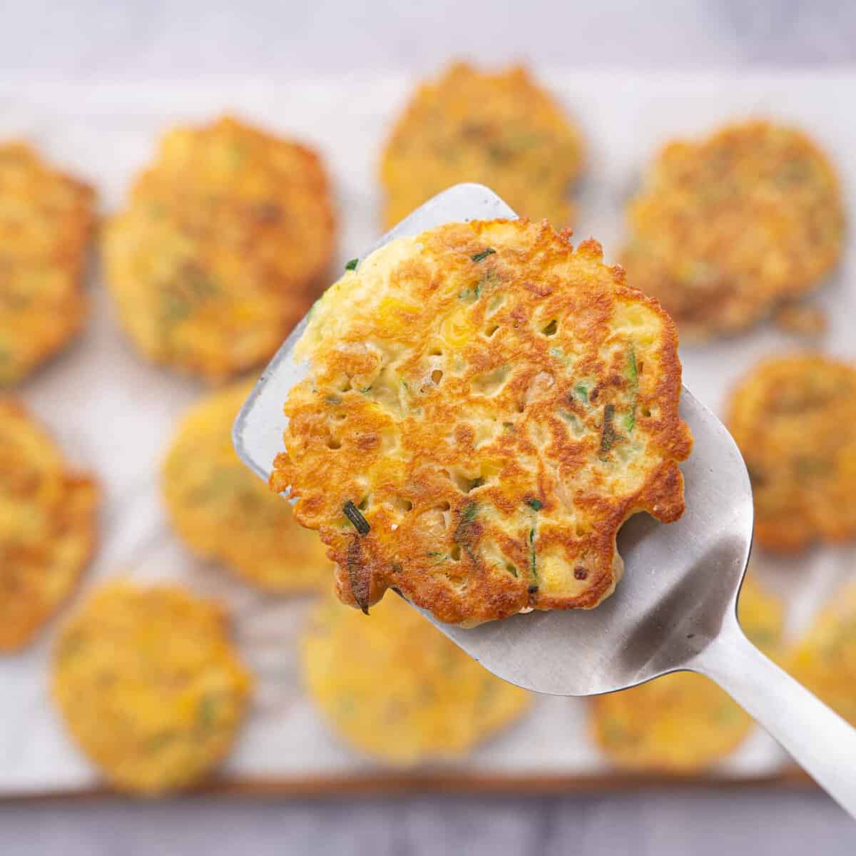 A golden brown chickpea fritter resting on a spatula, raised up above the rest of the fritters