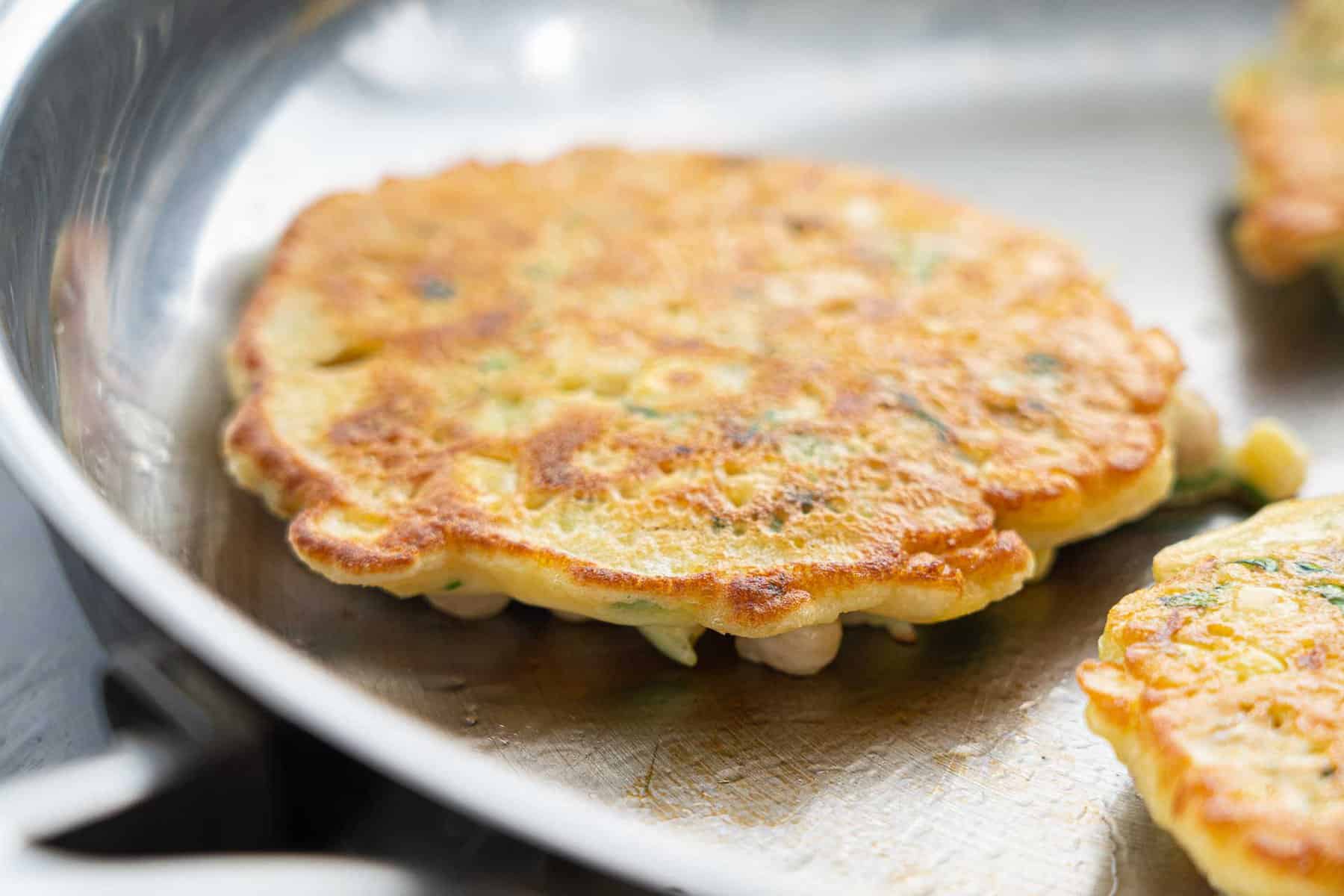 golden brown chickpea fritters flipped over in the frying pan