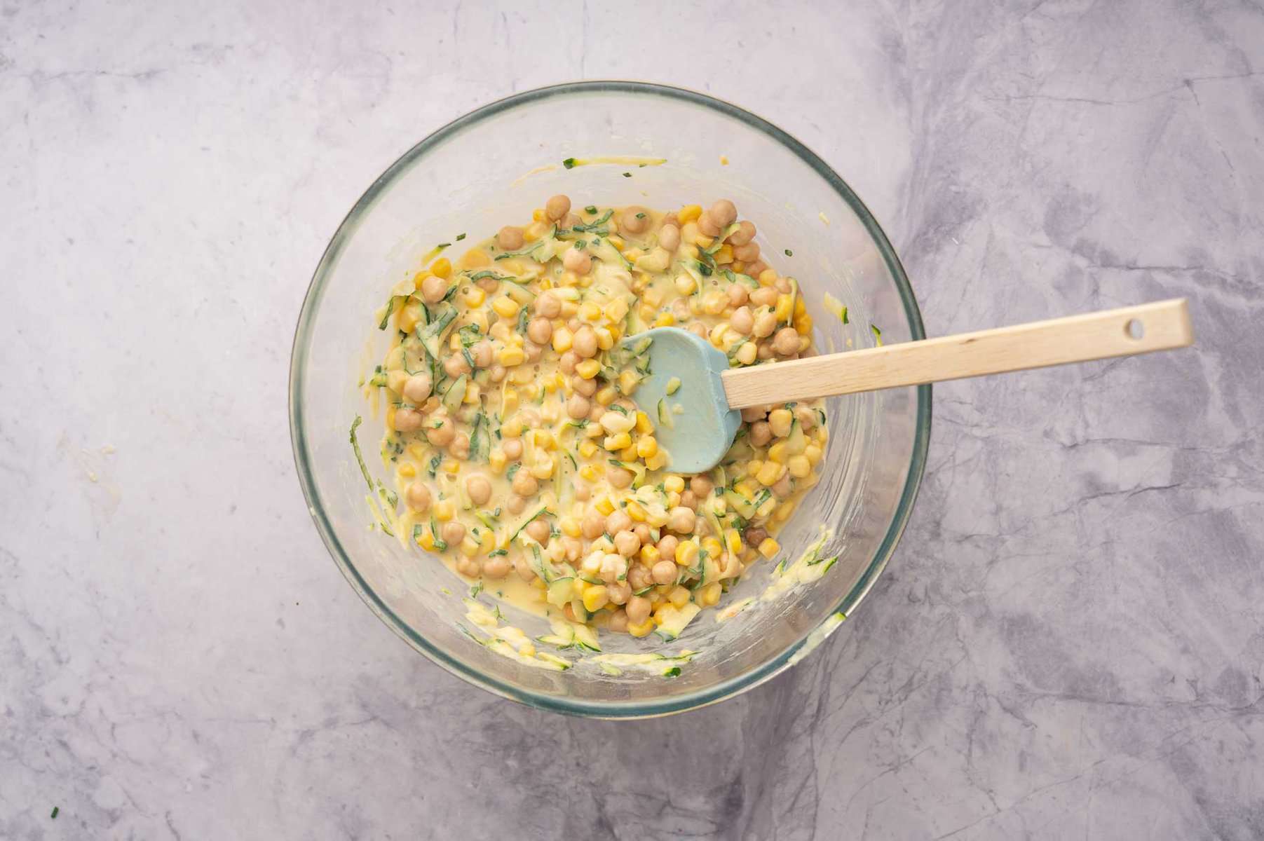 All of the ingredients in a bowl mixed together to create the chickpea fritter batter with a spatula resting against the side of the bowl