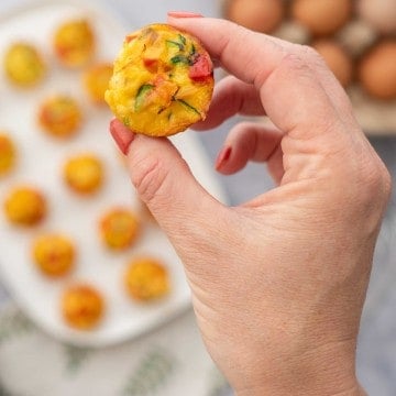 A mini egg muffin stuffed with colourful vegetables being held up to the camera.
