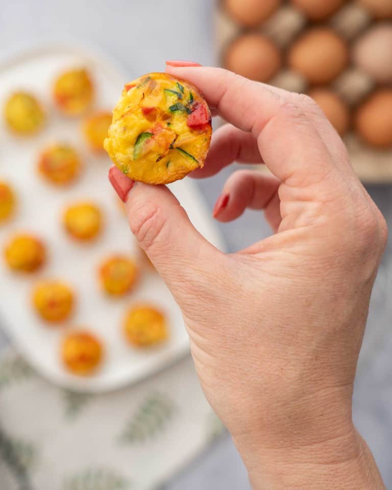 A mini egg muffin stuffed with colourful vegetables being held up to the camera.