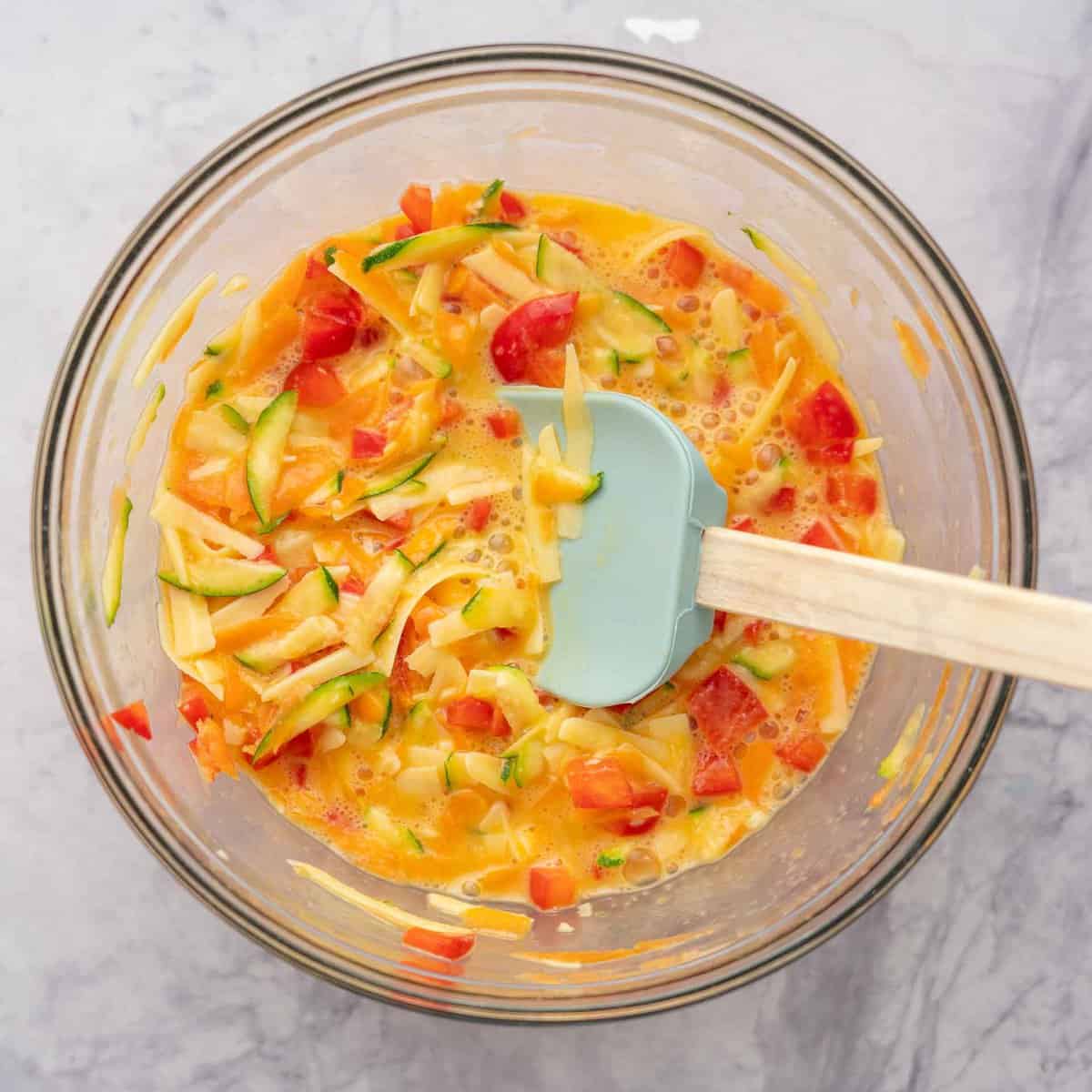 Glass mixing bowl of diced vegetables and whisked eggs.