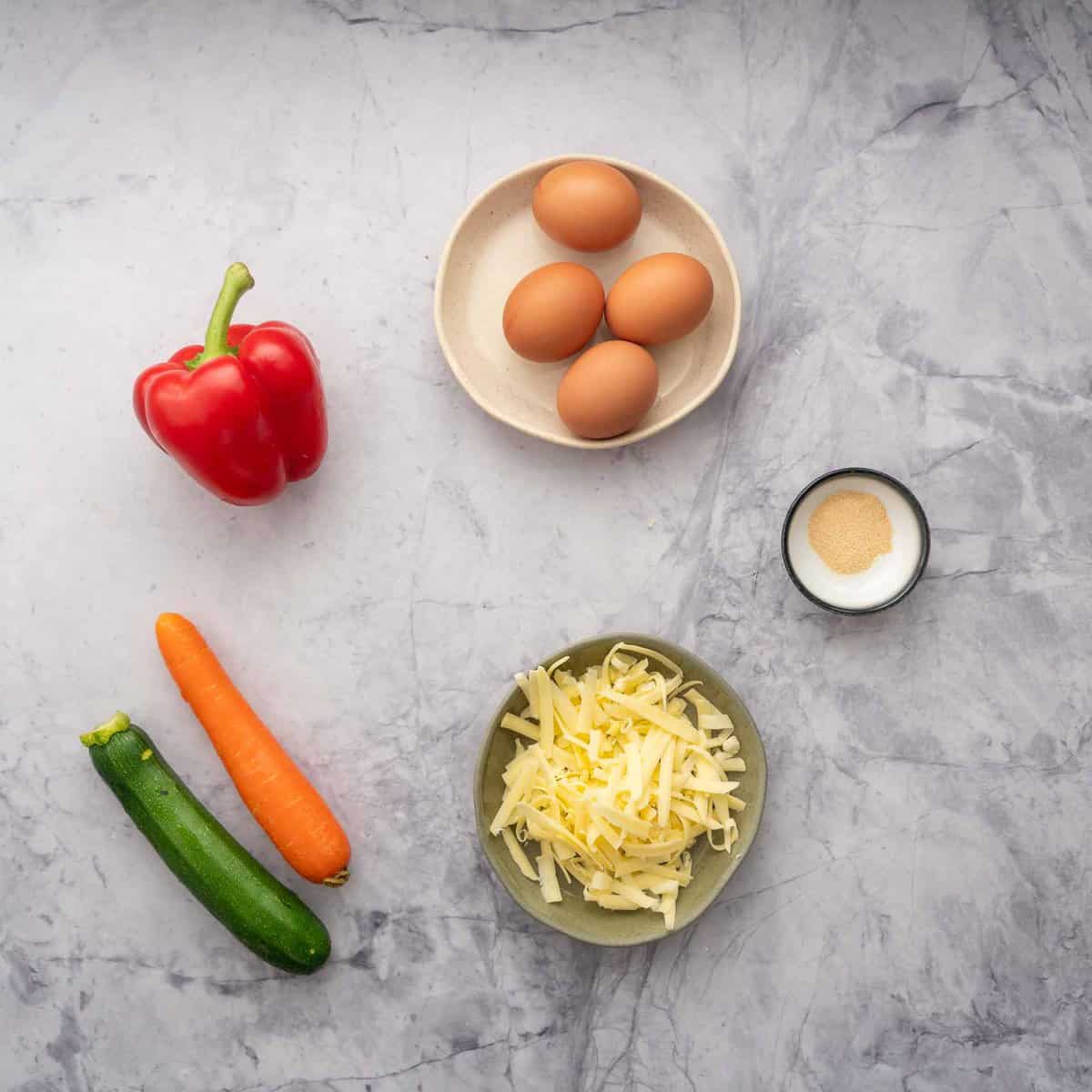 Eggs, capsicum, zucchini, carrot, cheese laid out on a bench top.