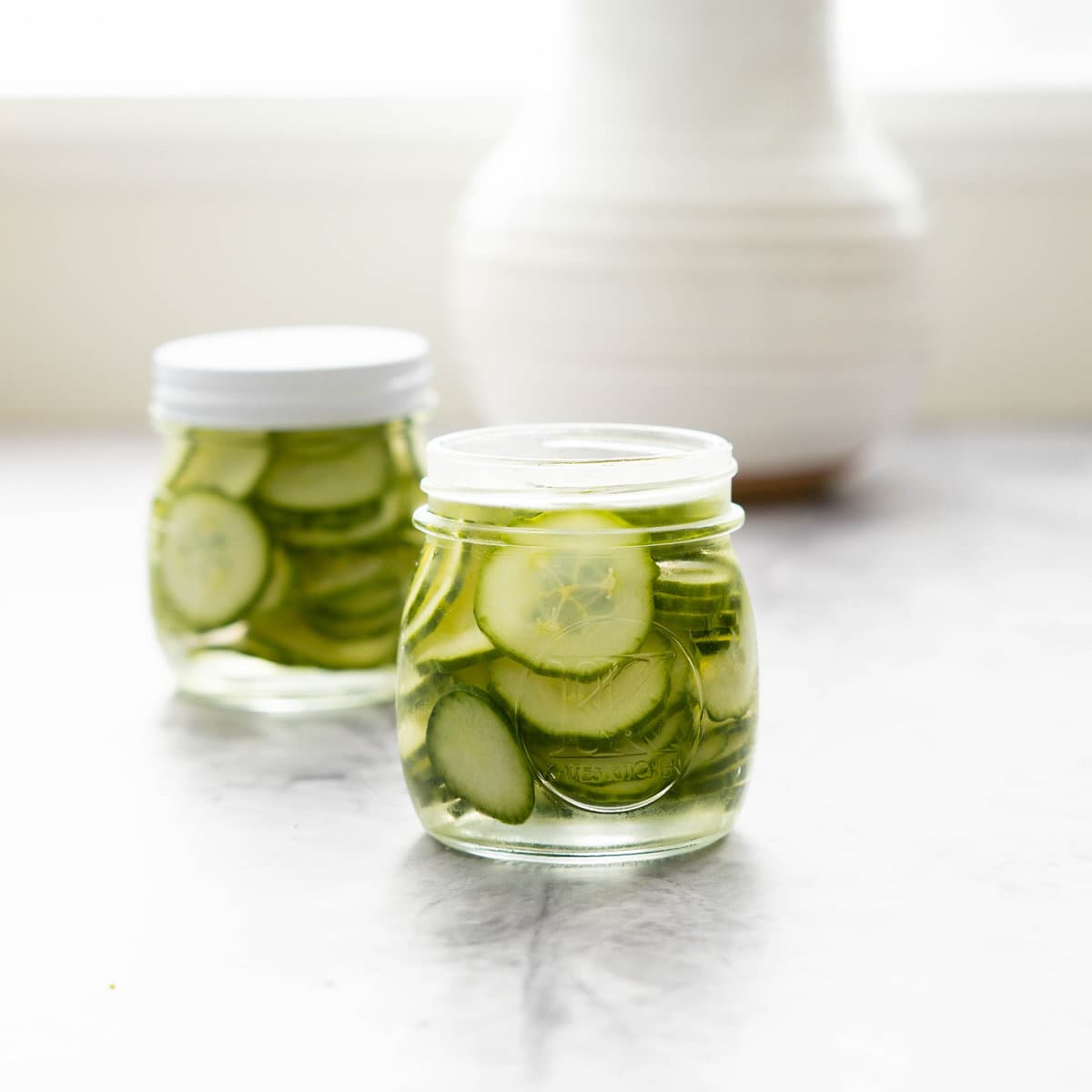 Cucumbers and brine poured into two jars sitting on bench top one with lid on and one off.