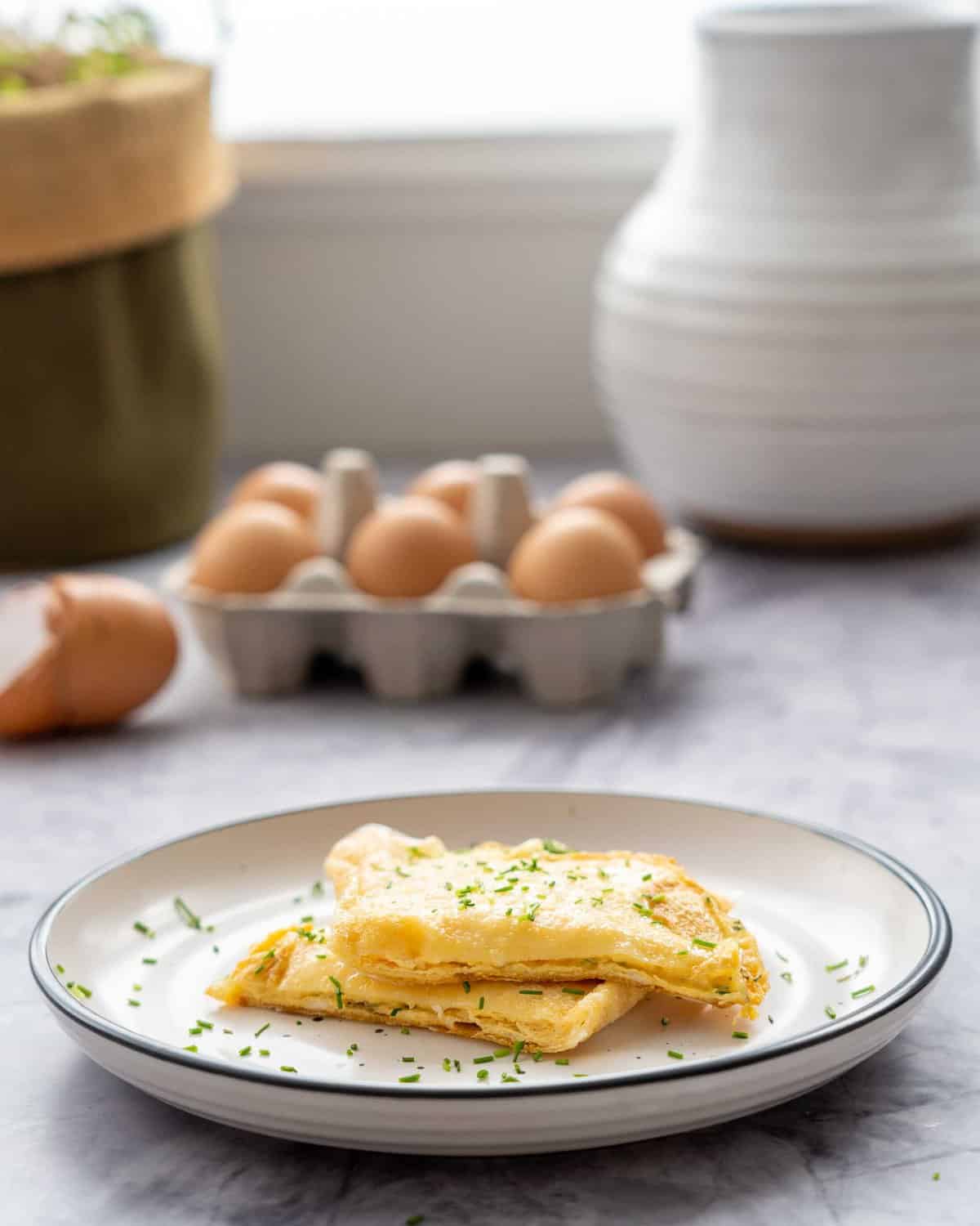 Cheese and chive omelette on plate on bench top with carton of eggs in background.