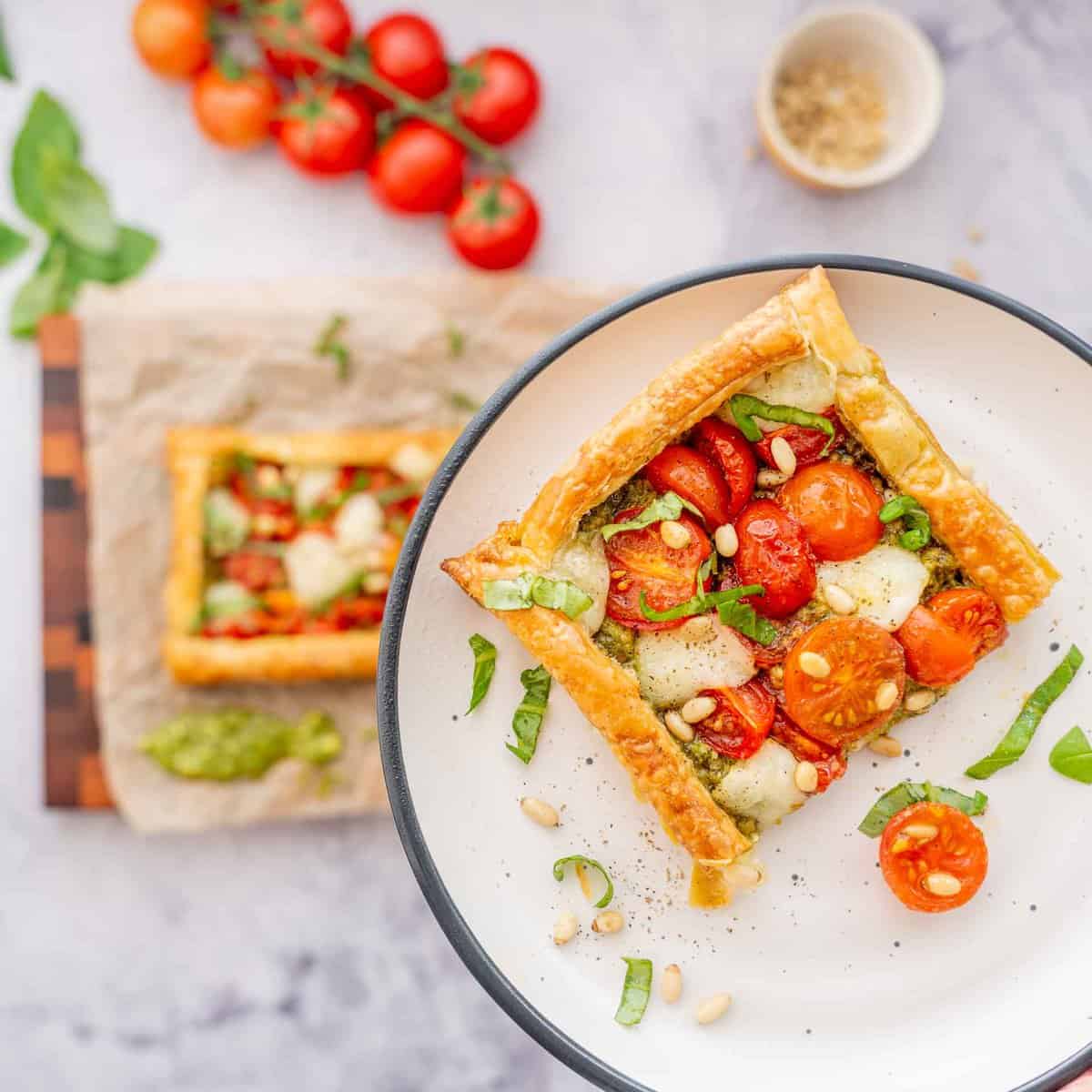 One slice of Tomato tart on a plate raised above the bench full of ingredients below.