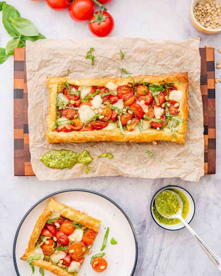 A tomato tart on a wooden chopping board next to a side plate with one piece of tomato tart on it.