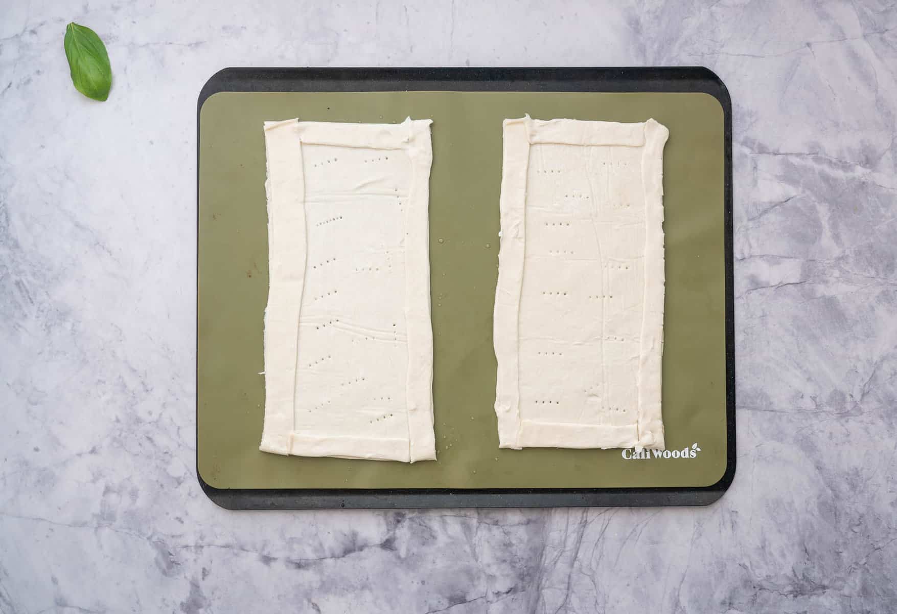 Sheets of puff pastry, shaped into two tarts sitting on baking matt on the bench