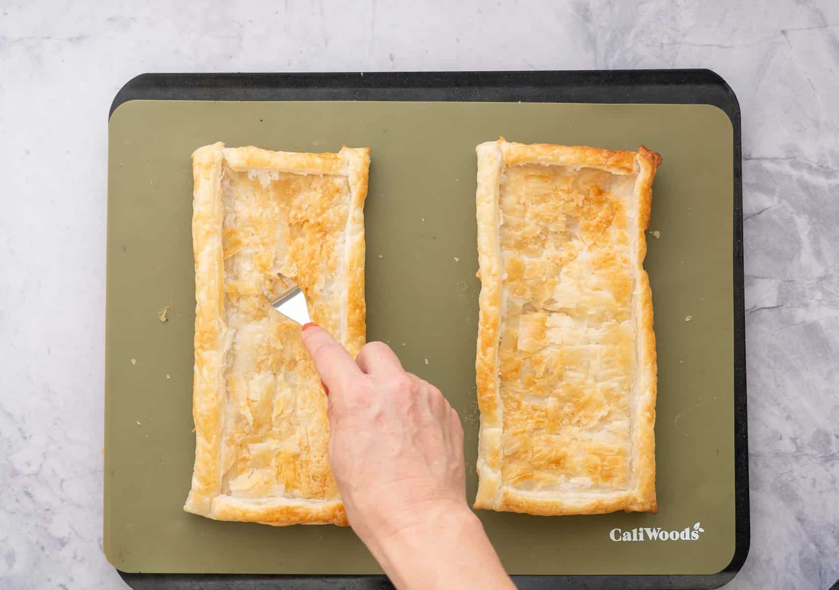 A hand pressing a fork into one baked tart case which is sitting on a baking tray on the bench
