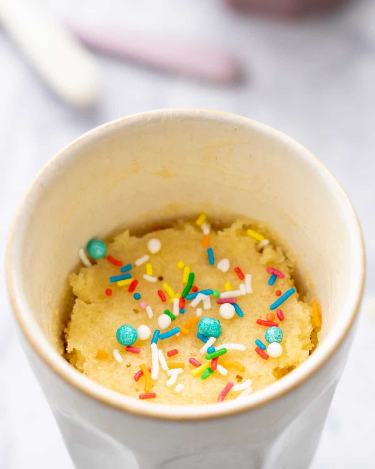 One mug showing the baked Vanilla Mug Cake with multicoloured sprinkles on top.
