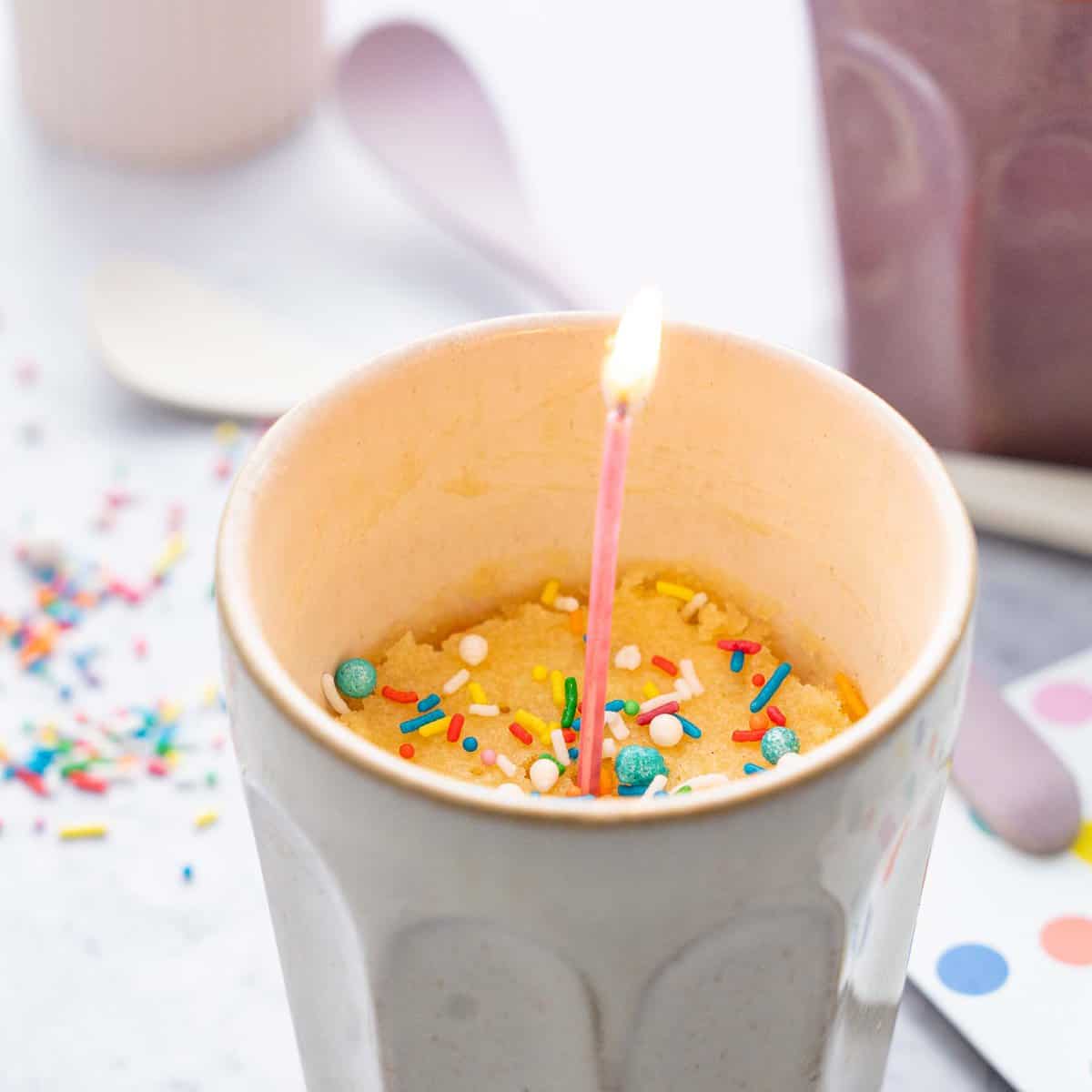 Vanilla mug in a cup with colourful sprinkles and a lit pink candle inside.