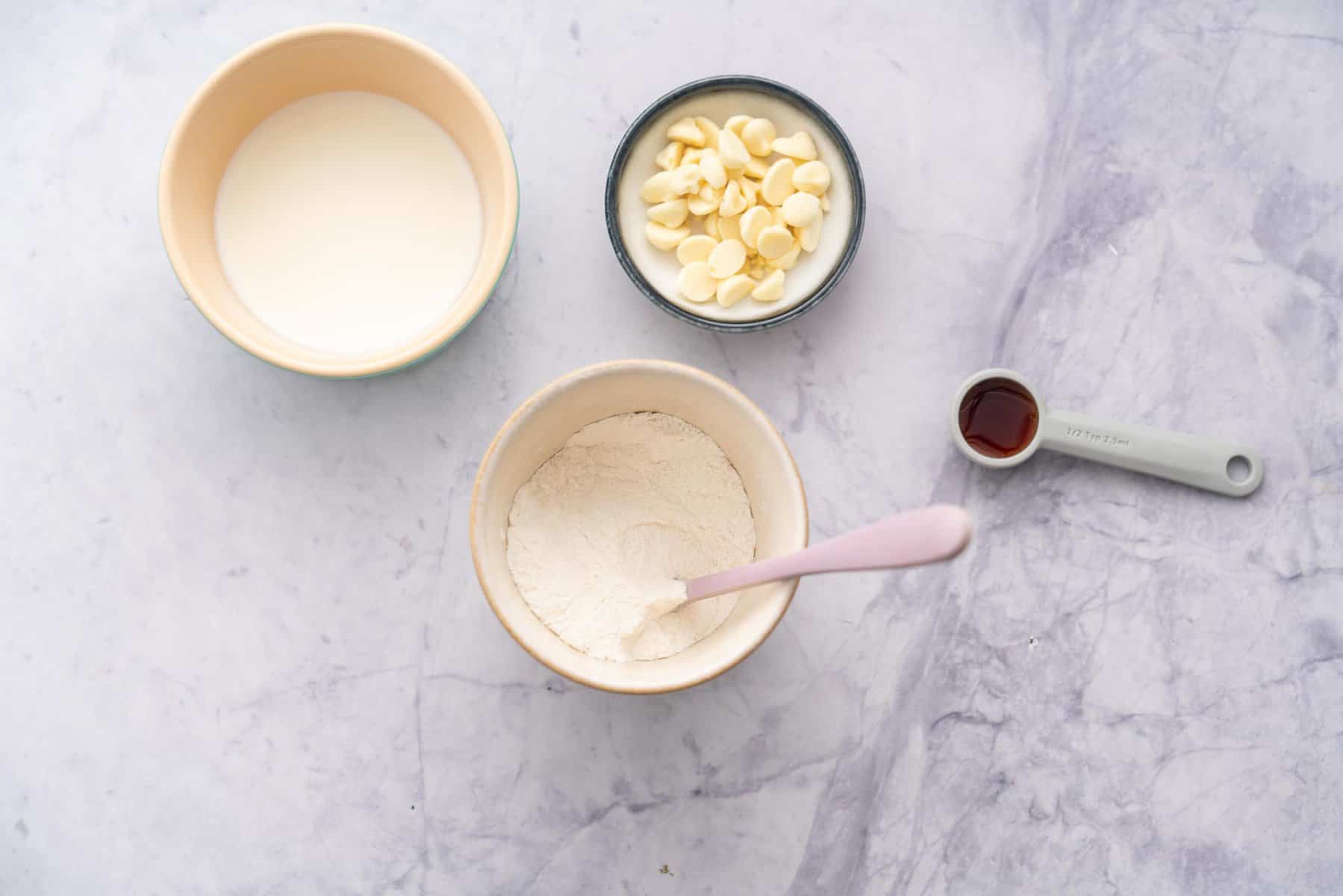 Ramekins individually filled with milk, self raising flour, white chocolate chips and vanilla essence laid out on the bench