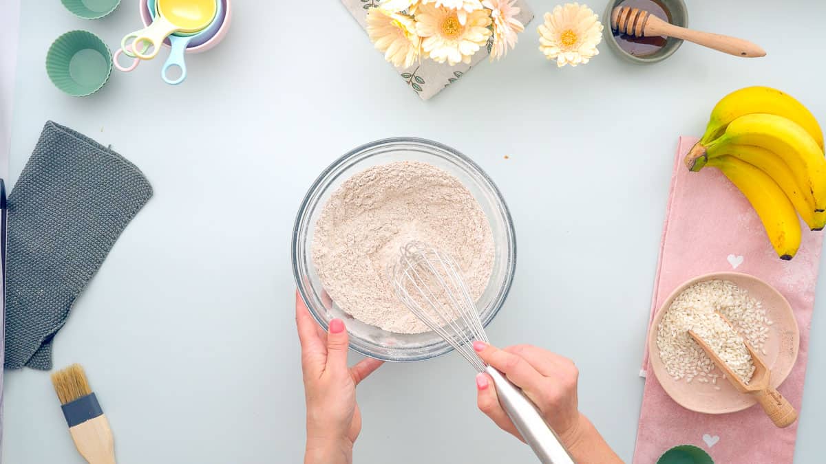 A glass mixing bowl of dry ingredients being combined with a whisk.