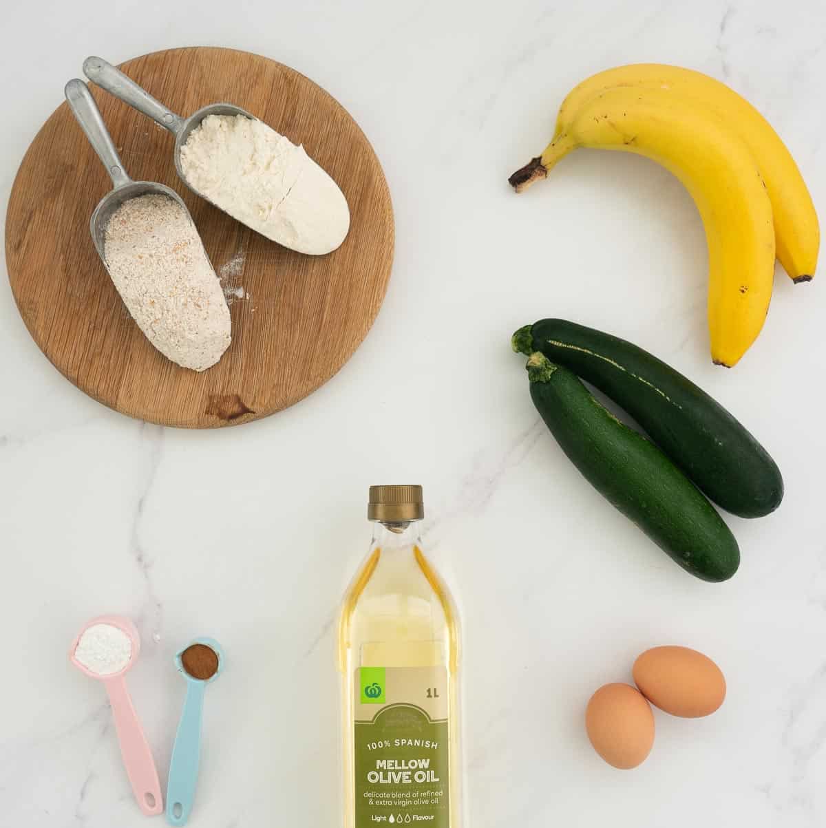 The ingredients to make banana zucchini bread laid out on a white marble bench top.