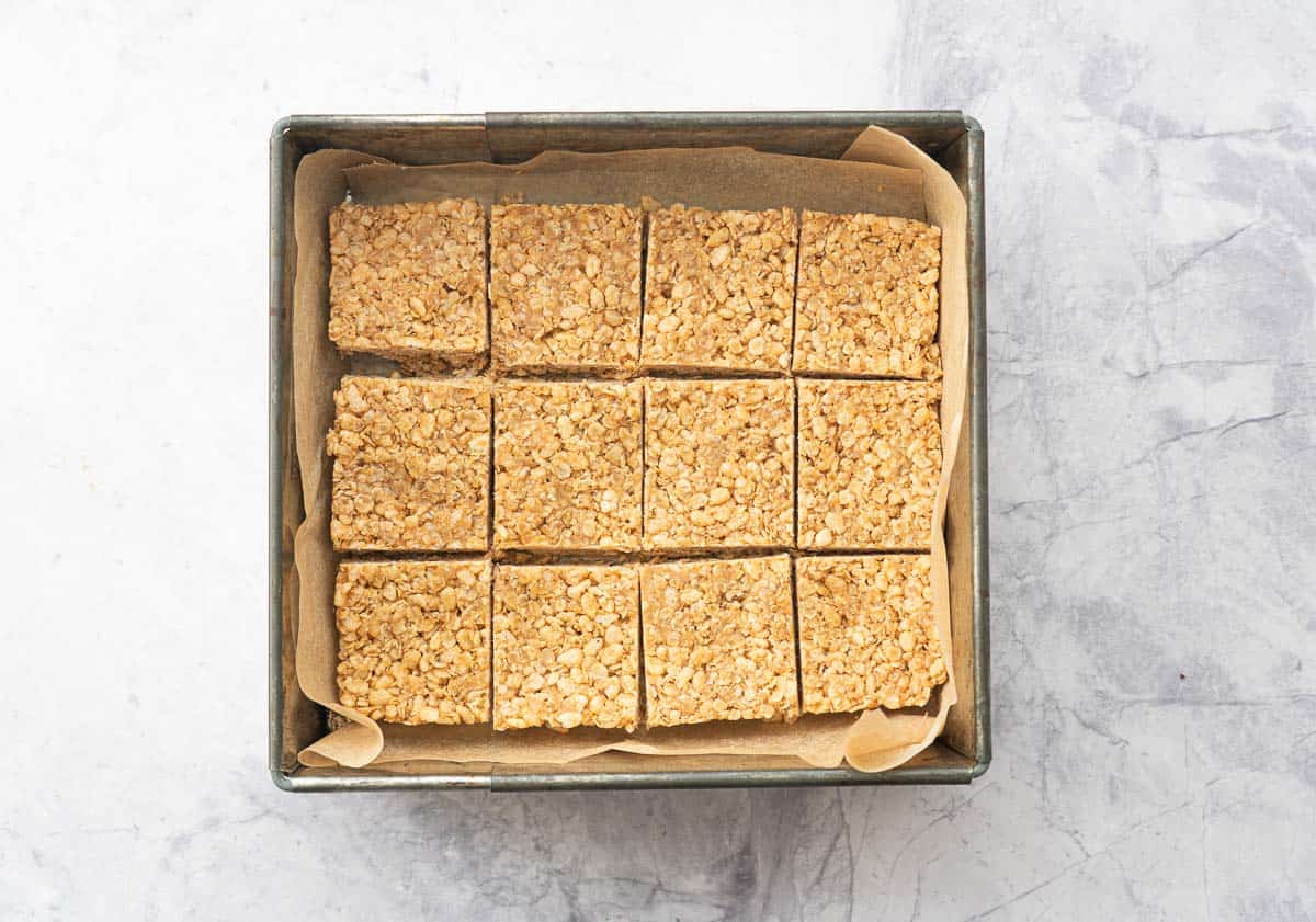 Twelve peanut butter rice krispie bars in a lined square cake tin.