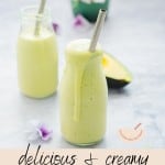 Two glass jars filled with Avocado Smoothie sitting on a bench with metal straws in each one with text overlay for pinterest.