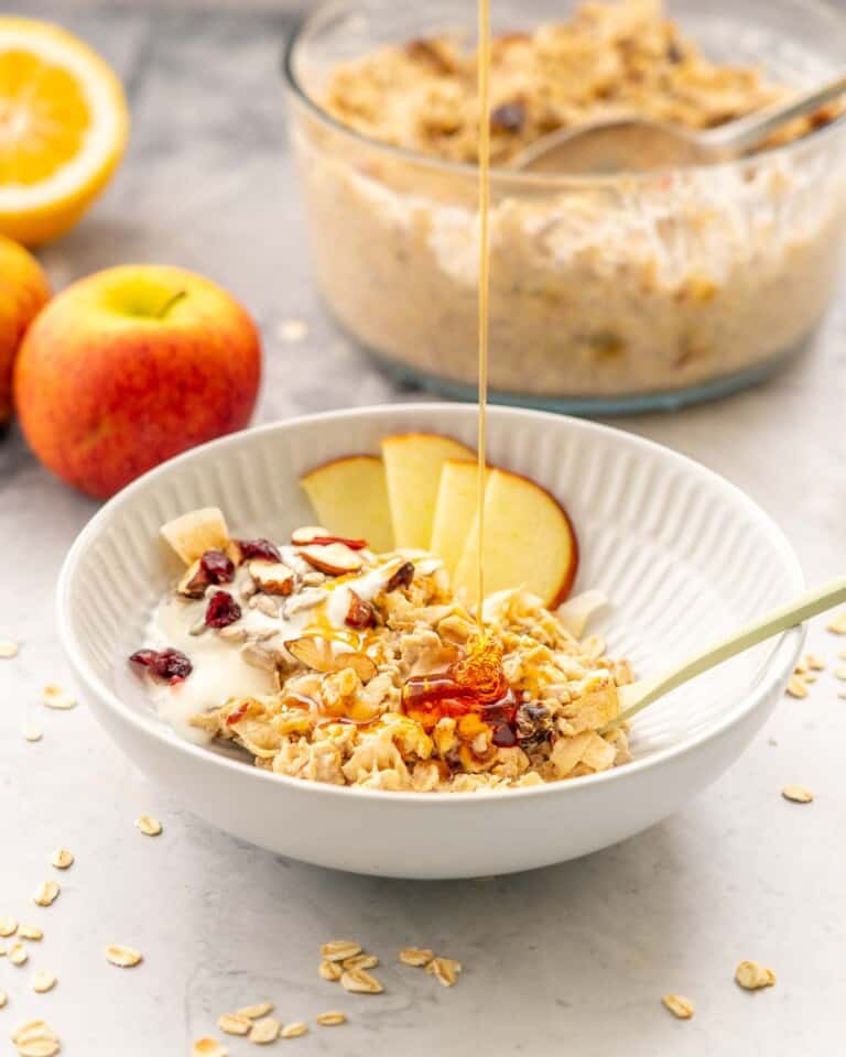 A bowl of bircher muesli, sliced apple and yoghurt being drizzled with honey.