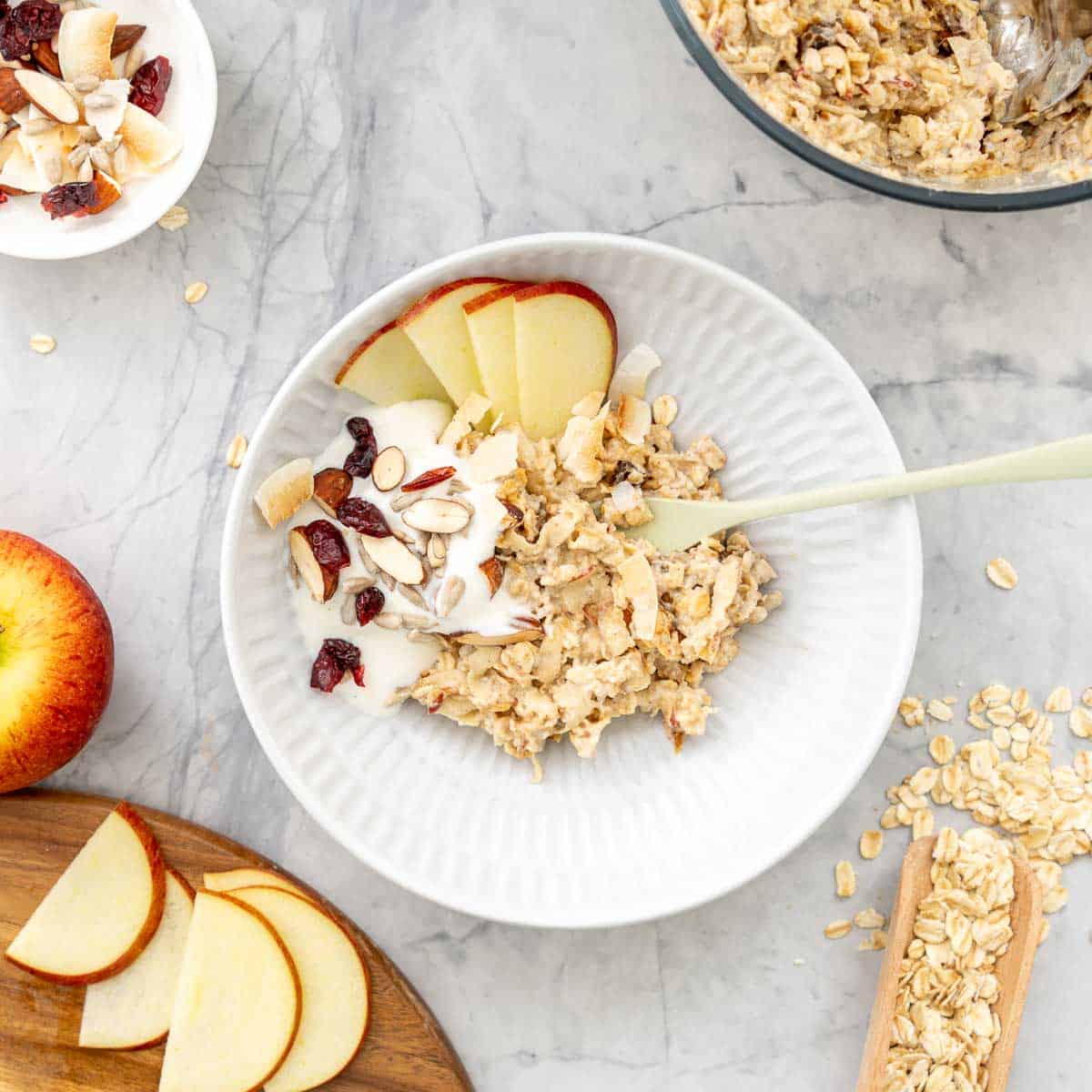 A bowl of bircher muesli served with thinly sliced apple and yoghurt.