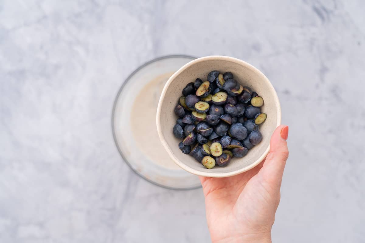 Fresh blueberry's cut in halves held up in a bowl over the whisked ingredients.