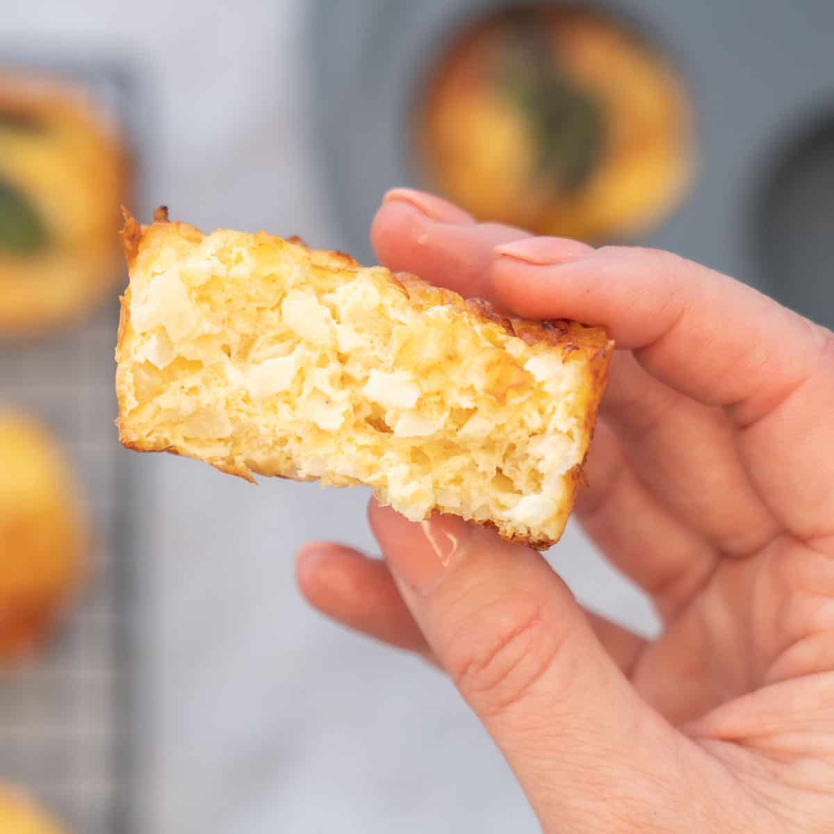A hand holding up half of a breakfast egg muffin above the bench