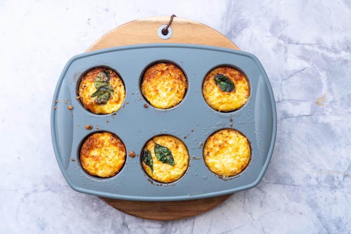 A tray of baked breakfast egg muffins sitting on a wooden chopping board on the bench