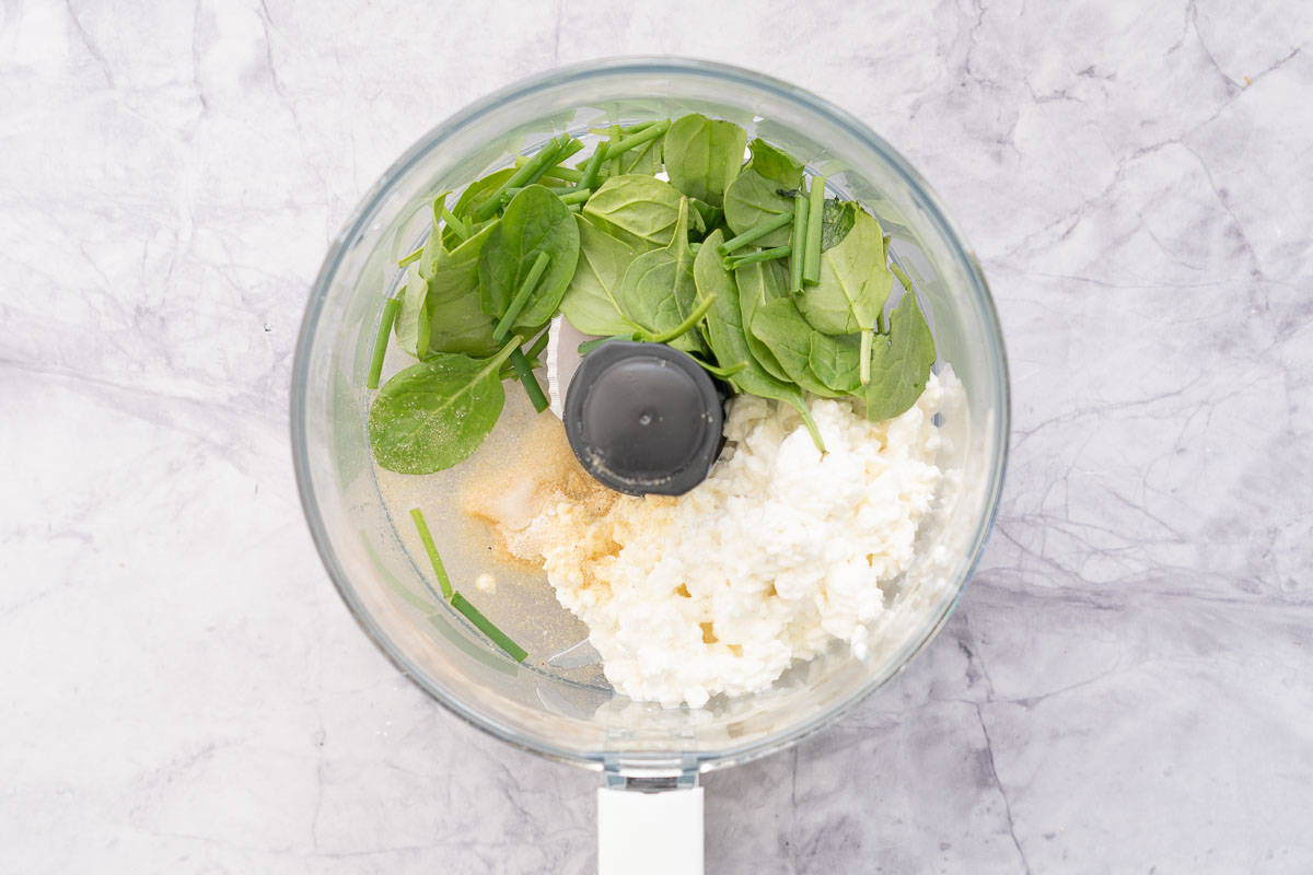 All the ingredients to make the cottage cheese dip added to a food processor which is sitting on the bench