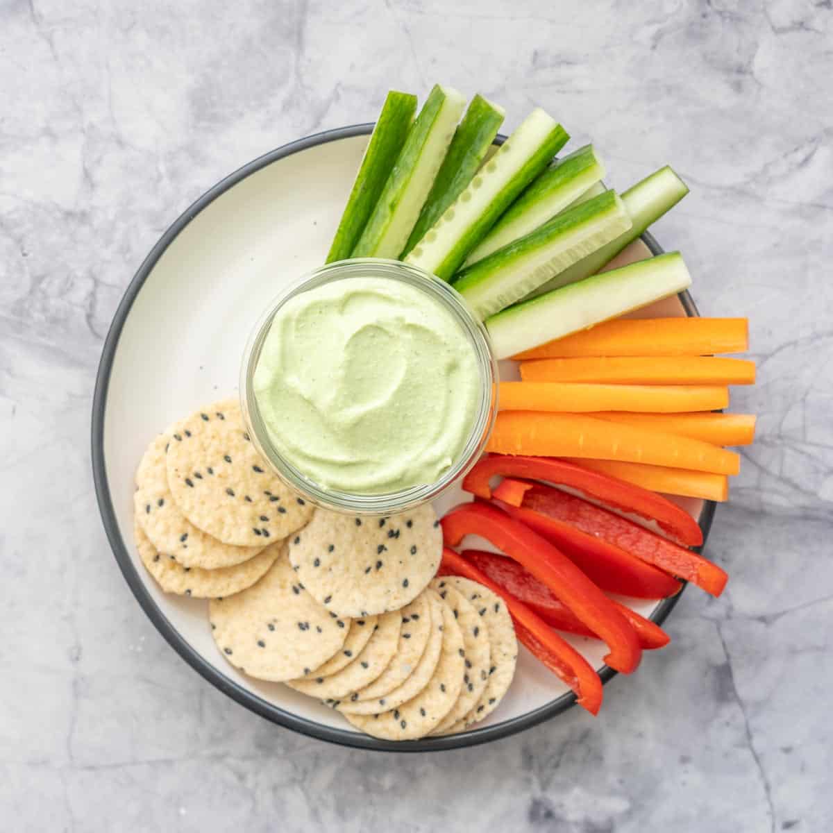 Cucumber, carrot and capsicum slices and crackers on a plate with a glass ramekin of cottage cheese dip