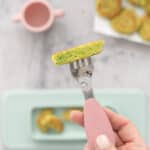 A fritter cut in half on the end of a fork, chunks of peas visible.