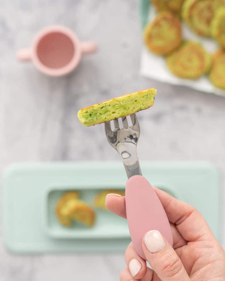 A fritter cut in half on the end of a fork, chunks of peas visible.