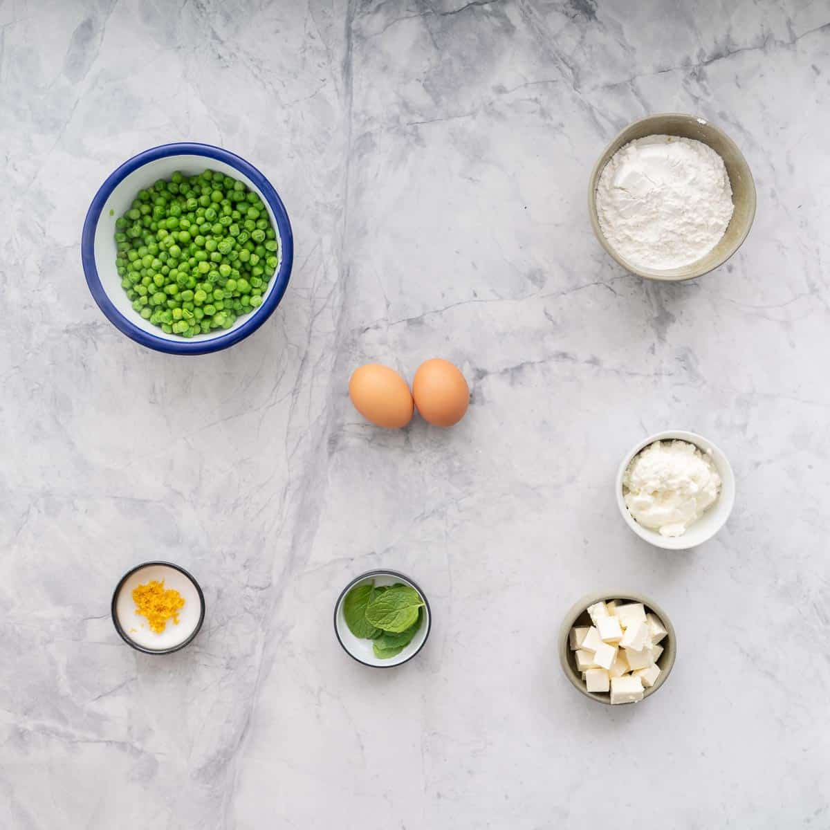 All the ingredients to make the pea fritters in ramekins laid on on the bench