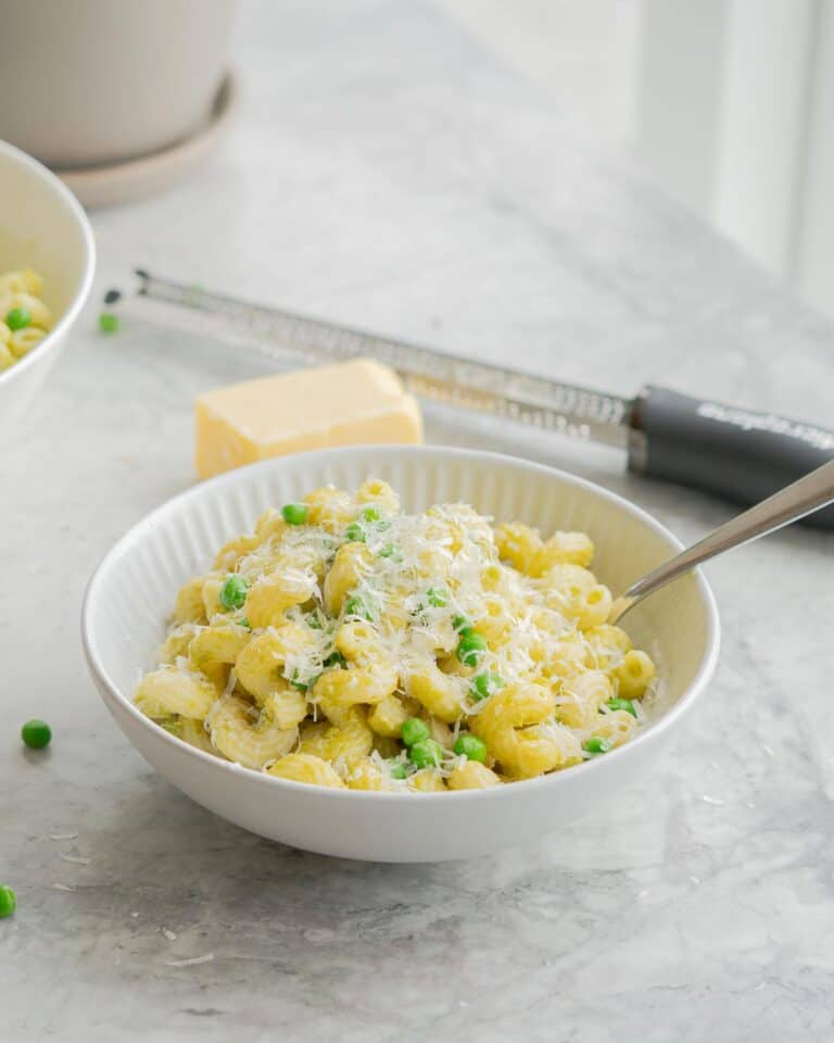 A bowl of spiral pasta with peas visible and parmesan cheese.