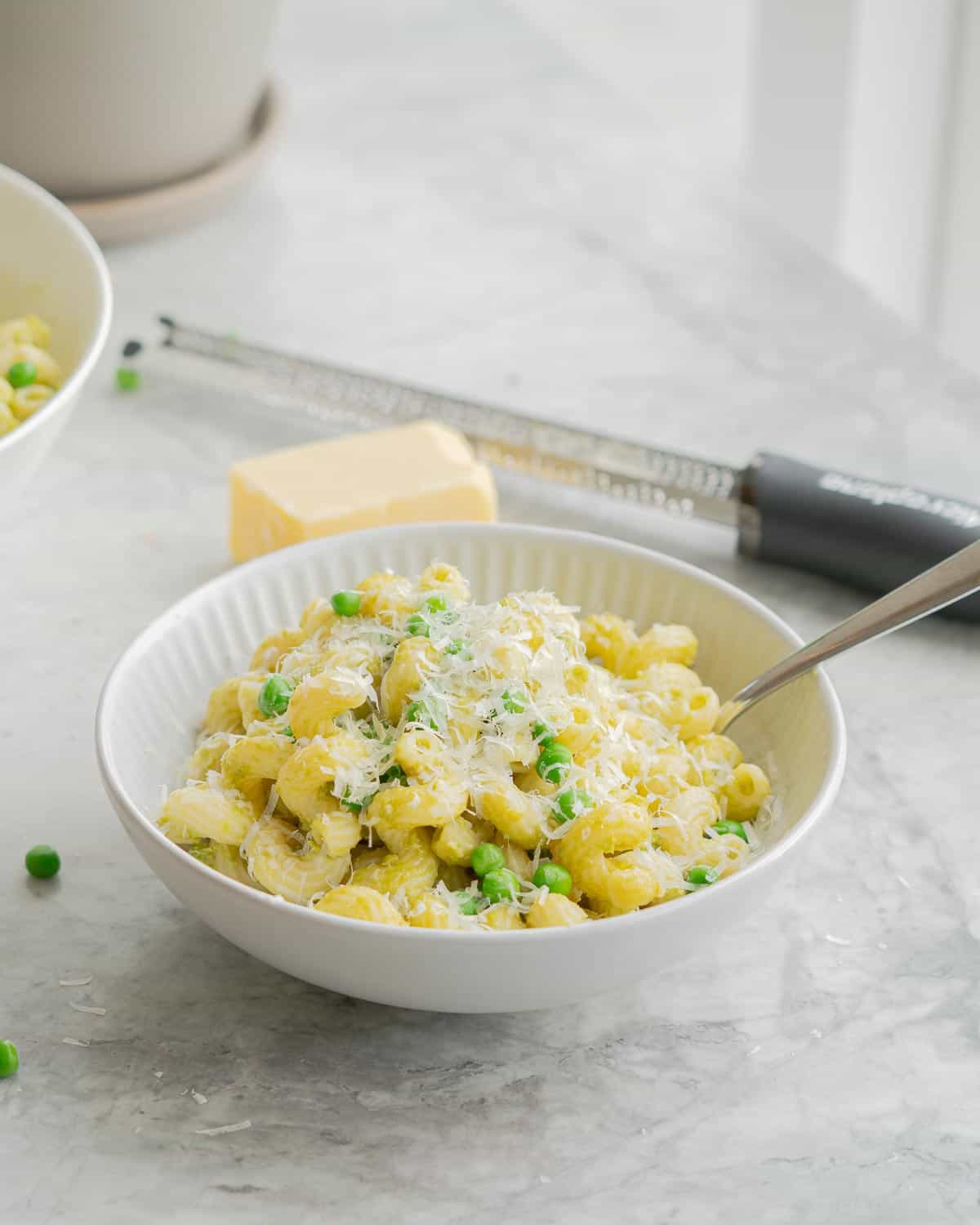 A bowl of spiral pasta with peas visible and parmesan cheese.