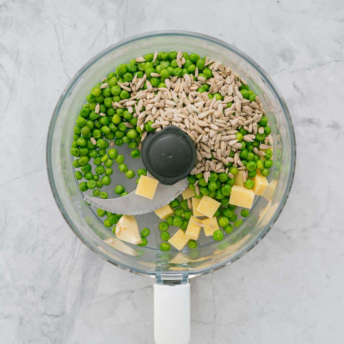 Peas, sunflower seeds and parmesan cheese and garlic in a food processor on the bench