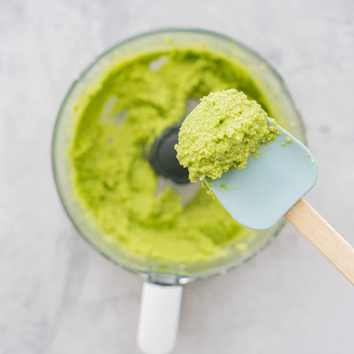 Blitzed ingredients in a food processor with a spatular of batter held above the bowl