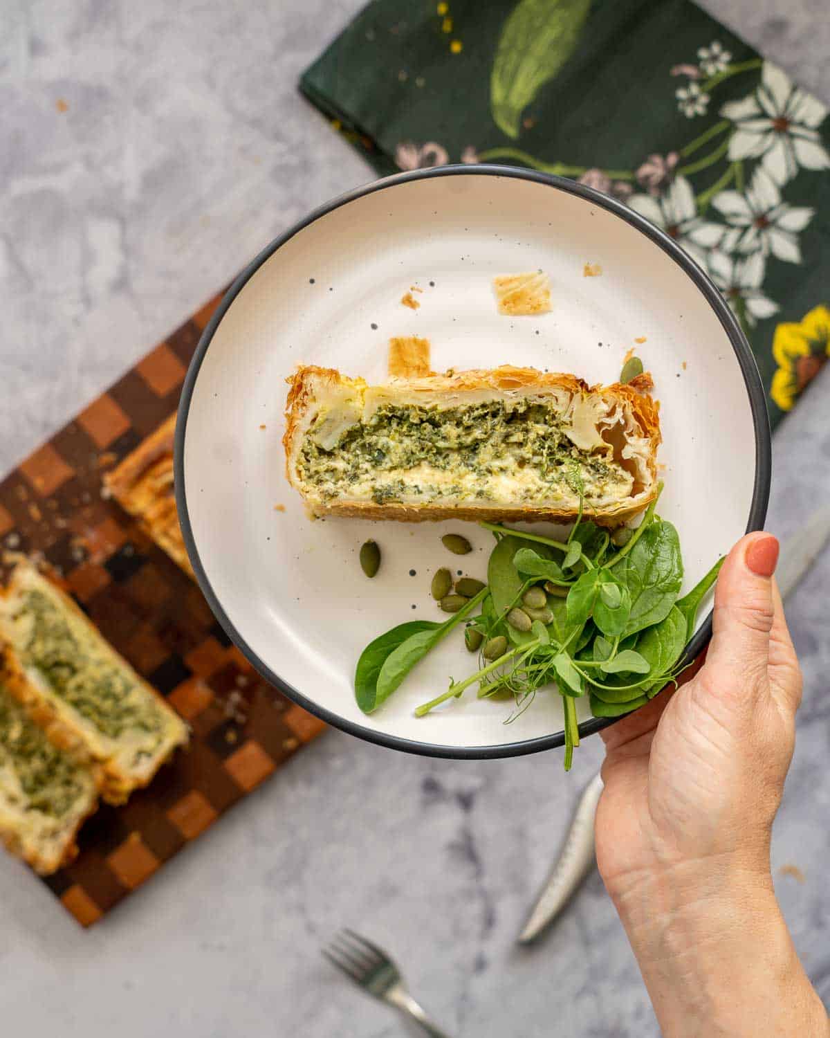 A plate with a slice of spinach cheese pie being held up to the camera.