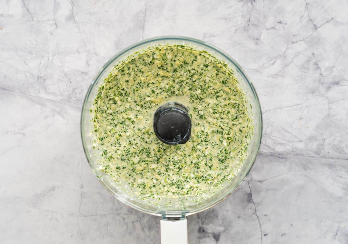 A food processor with blended spinach and cheese pie filling.