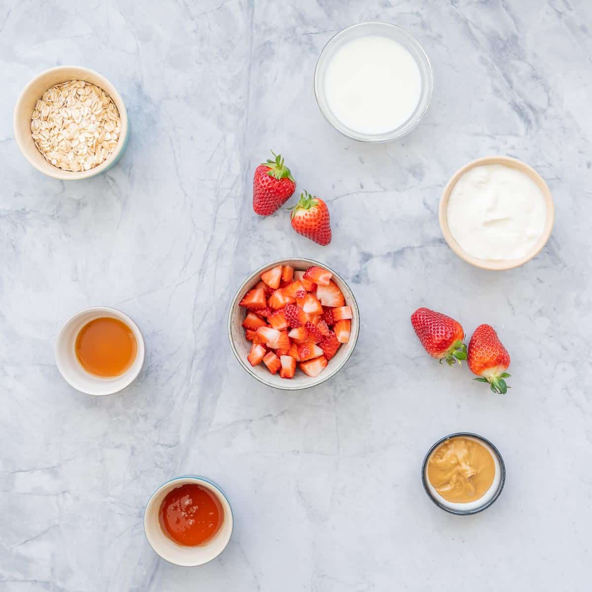 The ingredients to make strawberry overnight oats lad out on a bench top.