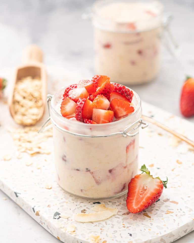 A glass jar filled with creamy oats topped with diced pieces of red strawberry.